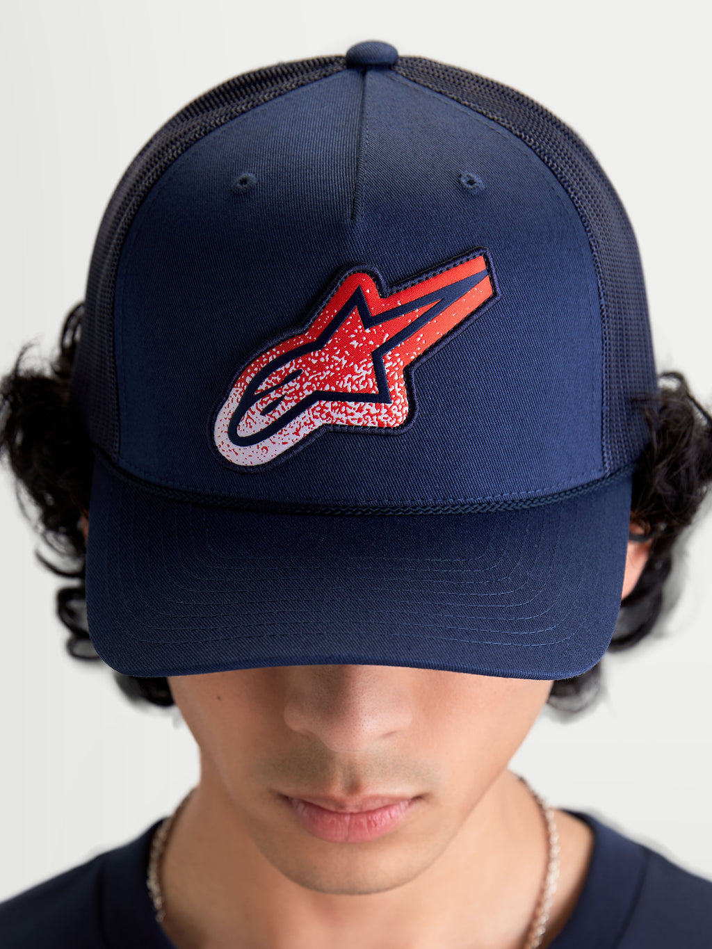 Alpinestars Meteorite Trucker Hat, Sportswear Mesh Cap for Men and Women, Navy Blue with Red and White Astars gravel texture logo patch, featuring a structured crown and curved bill, on-model front view.