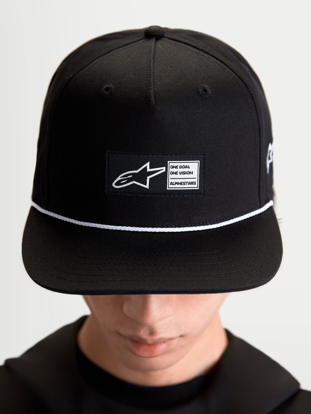Alpinestars Label Snapback Hat, Sportswear Lifestyle Cap, Unisex, Black and White, Cotton Twill, featuring a structured crown, flat bill, white cord accent, and a front woven label patch with signature Alpinestars branding, shown on-model.