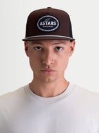 Alpinestars Hotlink Trucker Hat, Brown and Black Motorsport-Inspired Sportswear Cap, featuring a structured crown, flat bill with white rope detail, and front woven Astars Worldwide logo patch, shown on model.