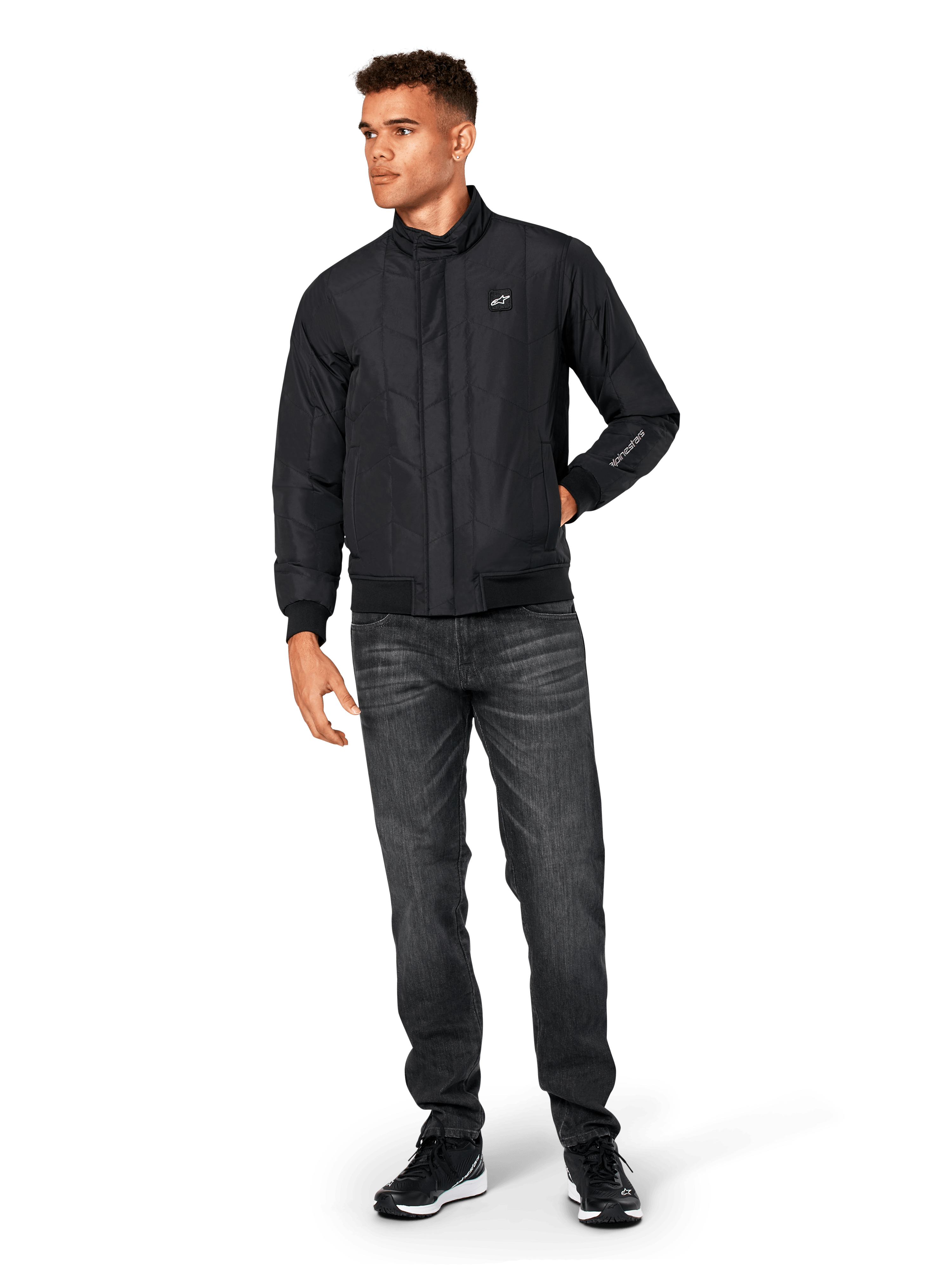 Alpinestars Precedent Jacket, Quilted Sportswear Jacket, Black, worn with dark grey jeans and black sneakers, featuring an angled quilt pattern, low track collar, rib-knit cuffs and hem, with a white logo patch on the chest and sleeve embroidery.