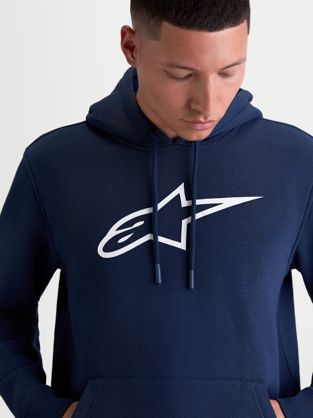 Alpinestars Ageless V3 Hoodie, Men's Sportswear Pullover Fleece, Navy Blue and White, featuring a large white embroidered Alpinestars chest logo, self-lined hood with dipped drawcord tips, and soft fleece construction for casual motorsport lifestyle wear.