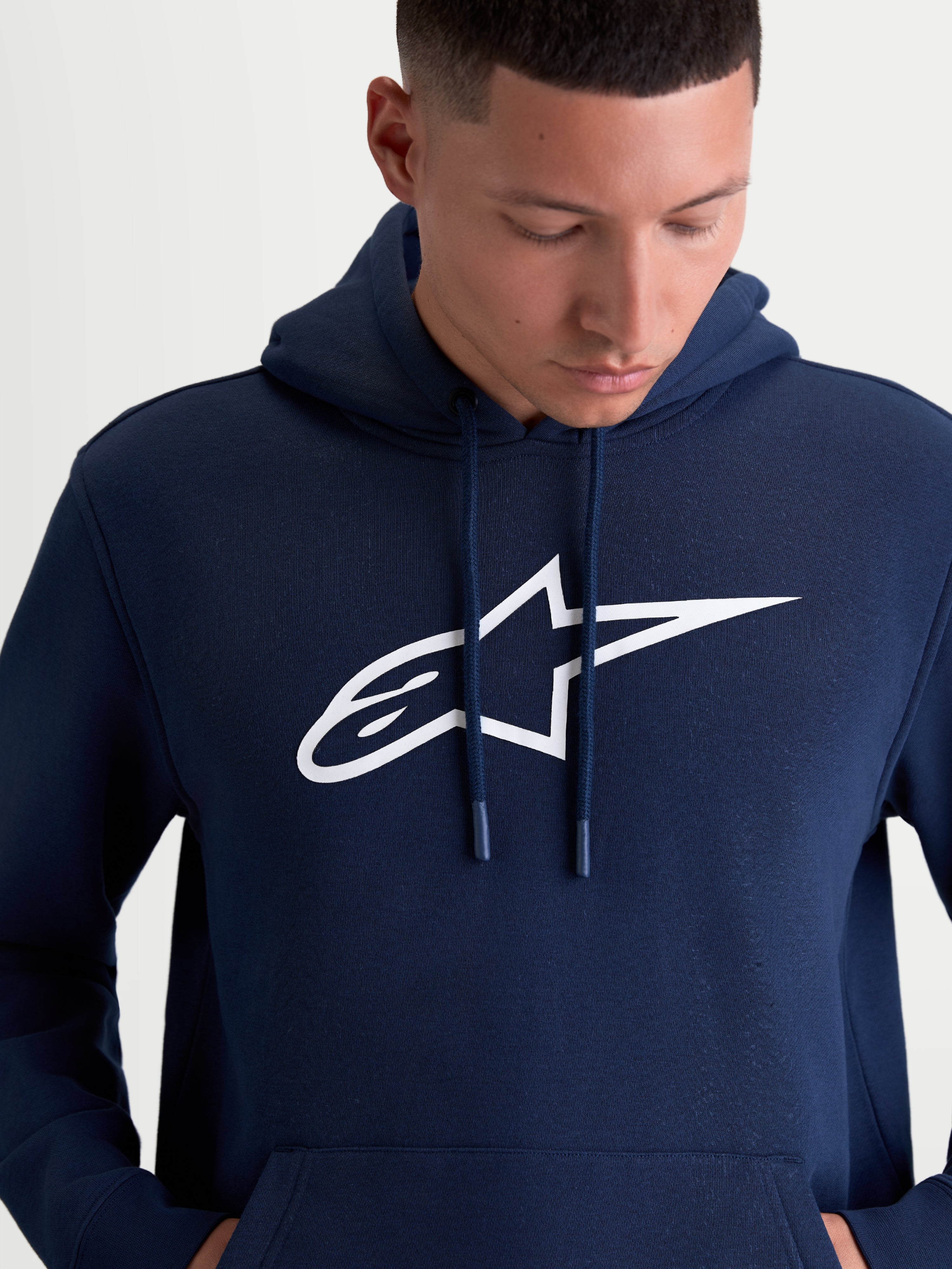 Alpinestars Ageless V3 Hoodie, Men's Sportswear Pullover Fleece, Navy Blue and White, featuring a large white embroidered Alpinestars chest logo, self-lined hood with dipped drawcord tips, and soft fleece construction for casual motorsport lifestyle wear.