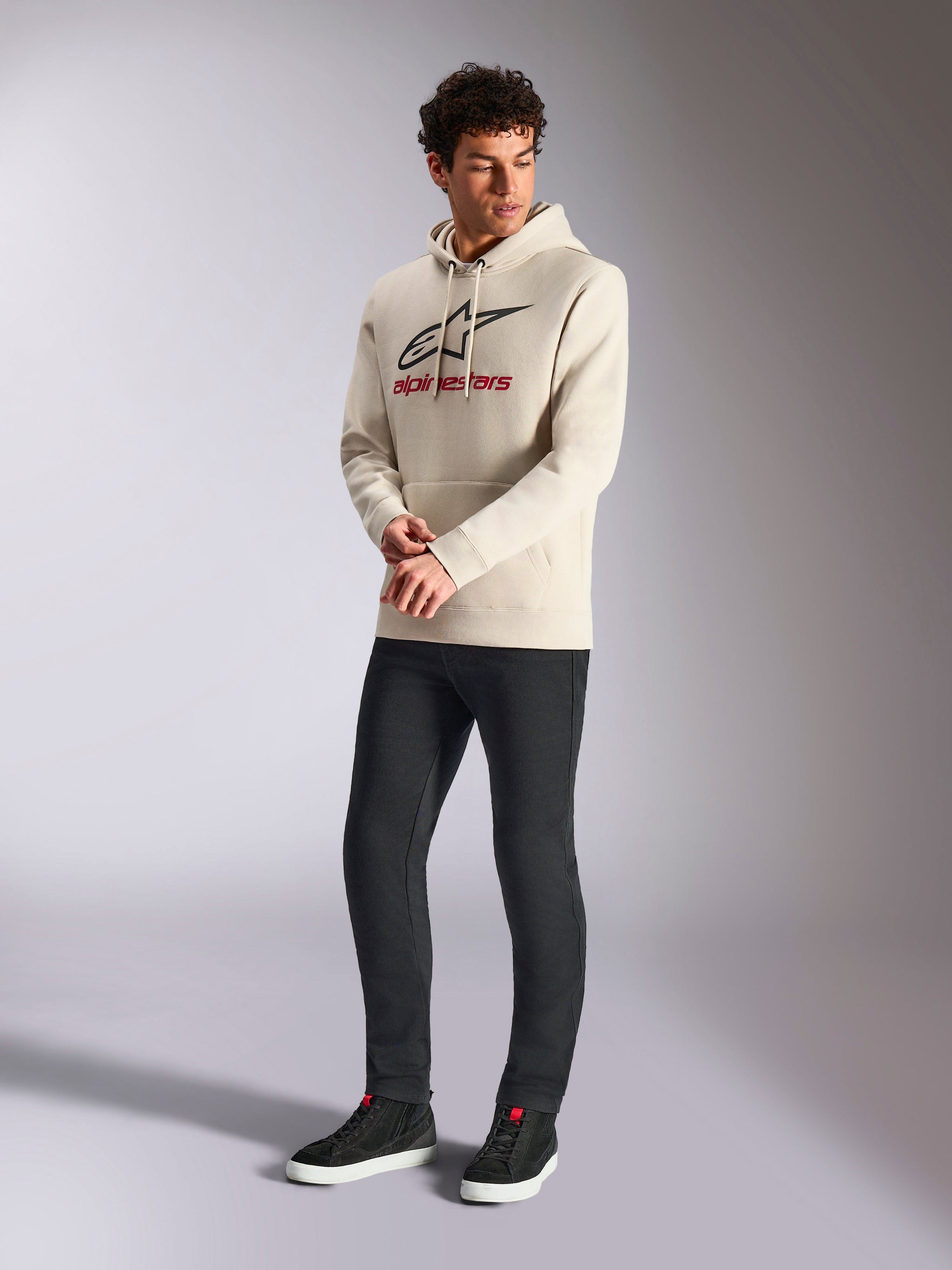 Alpinestars Always V3 Hoodie, off-white pullover fleece hoodie, front linear logo with black star and red branding, worn by a male model with black pants and black sneakers, casual motorsport streetwear
