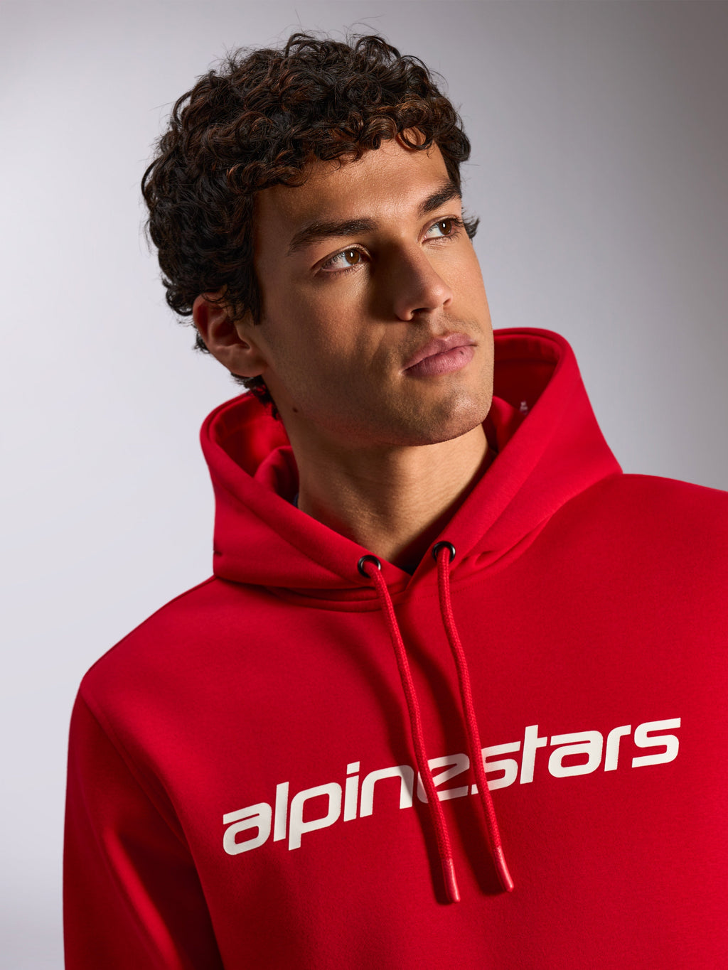 Alpinestars Linear Wordmark V3 Hoodie, red casual pullover fleece, white Alpinestars wordmark on chest, drawstring hood with dipped tips, lifestyle shot of male model