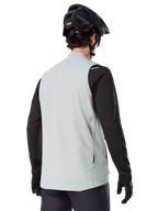 Alpinestars A-Dura Thermal Vest, Titanium Gray, rear view of model wearing a black long-sleeve jersey and MTB helmet, minimalist design with small red star logo on the back, lightweight insulated cycling gilet for off-road riding