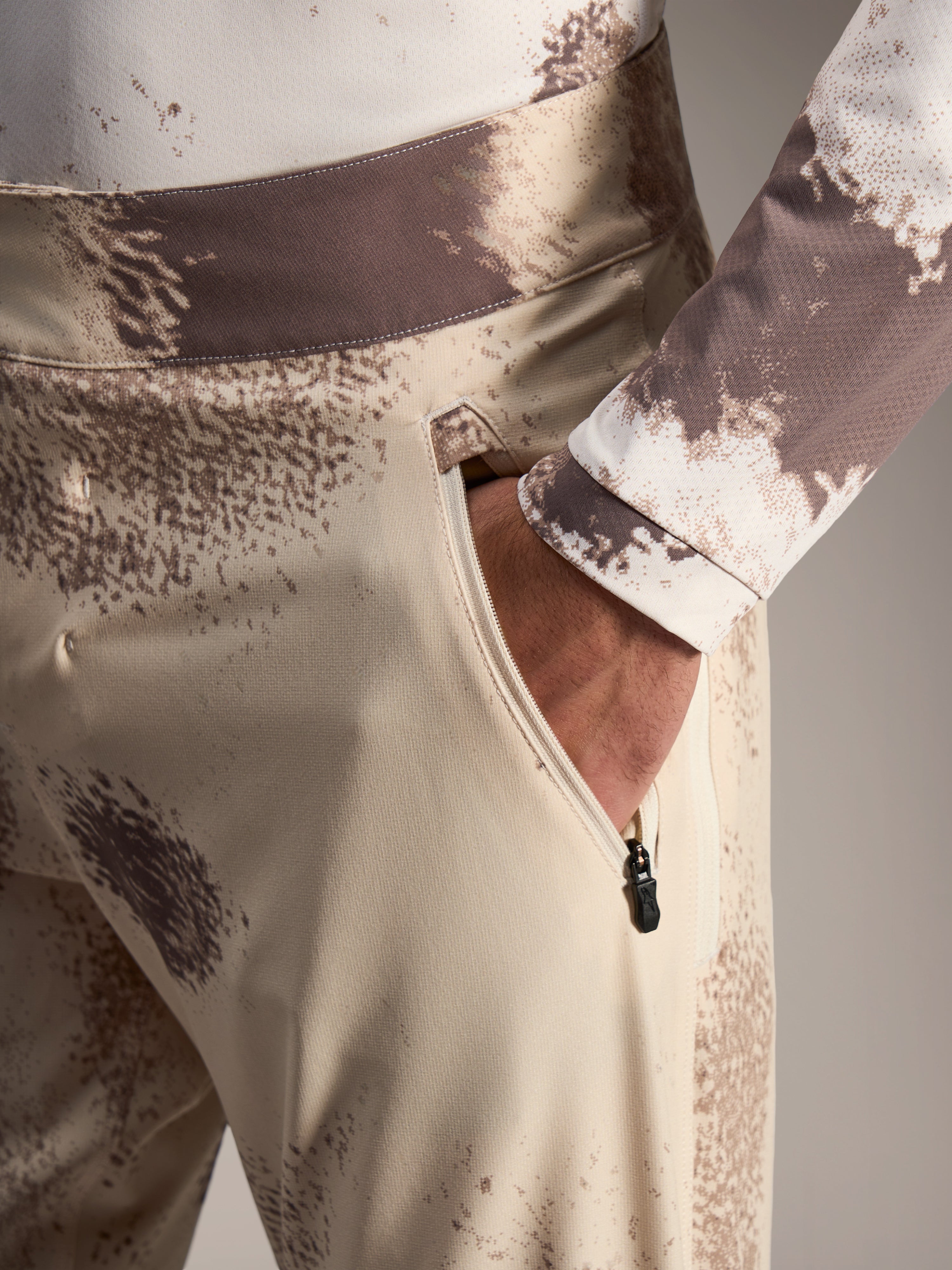 Alpinestars A-Dura Ride Shorts in Sand Camo, showing a zippered side pocket and durable 4-way stretch MTB fabric.
