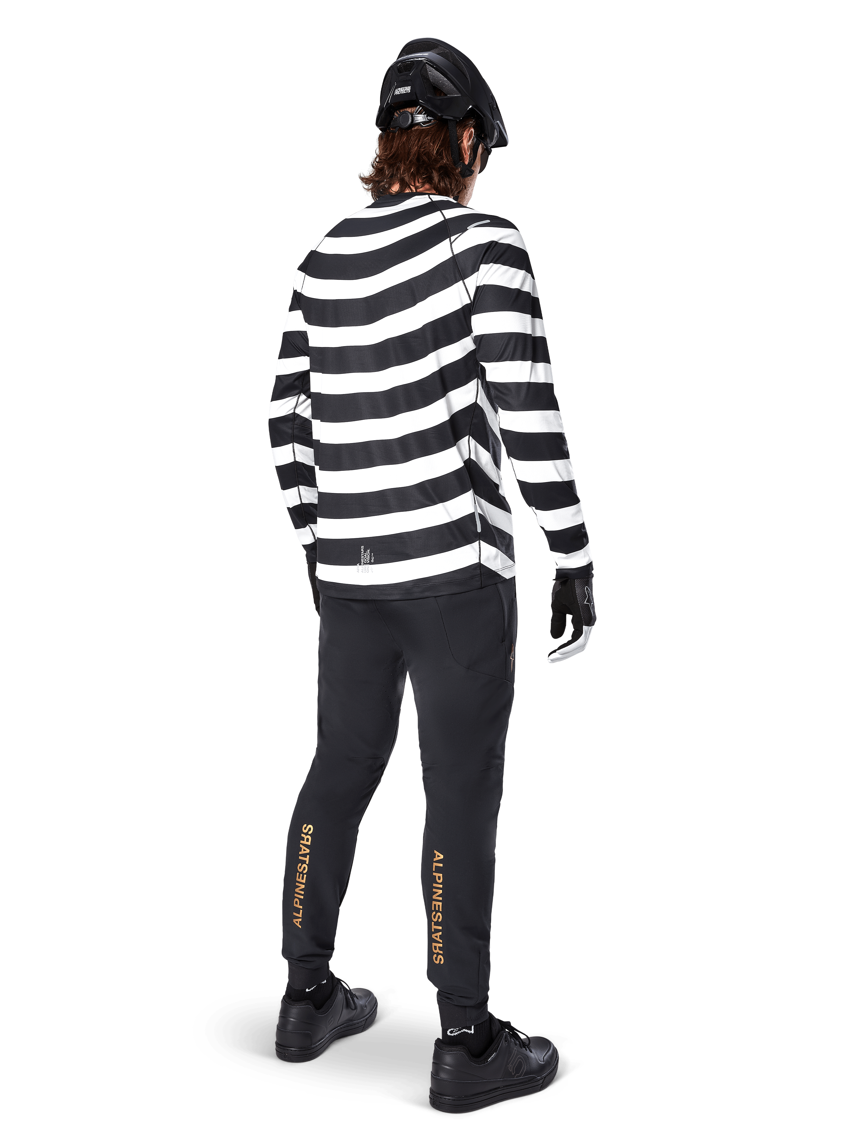 Alpinestars A-Aria Elite Pants, Black MTB Pants, featuring gold vertical logo on the calves, worn by a rider with a black and white striped long-sleeve jersey, black helmet, and black shoes, rear view showing performance fit and trail-ready design