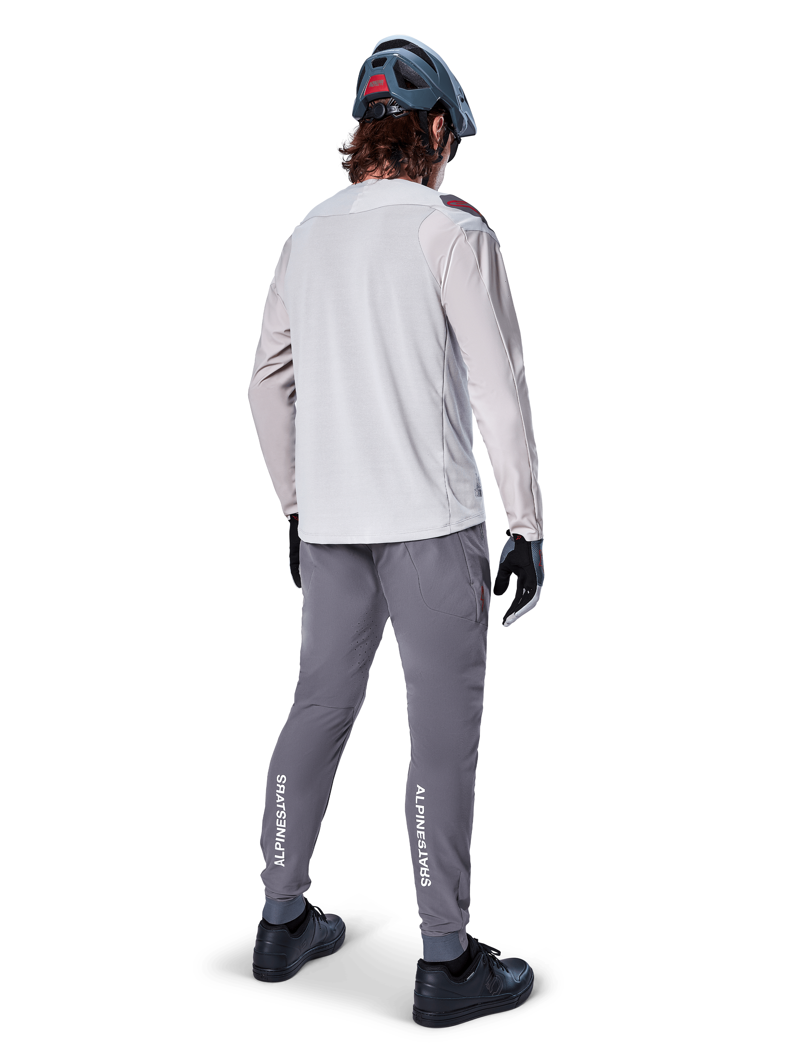 Alpinestars A-Aria Elite Pants, MTB Cycling Pants, Dark Gray, rear view of a rider wearing a full outfit, featuring white Alpinestars branding on the lower legs, performance fit with laser perforations, paired with a light gray long-sleeve jersey and gray MTB helmet