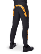 Alpinestars A-Supra Race Pants, Black MTB Pants, Rear view featuring large orange Alpinestars wordmark across the back yoke, orange logo on the lower leg, performance fit with zippered pocket, worn with black shoes