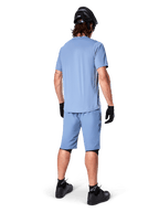 Rear view of a mountain biker wearing Alpinestars A-Dura Shorts in Infinity Blue, matching short-sleeve jersey, black helmet, black gloves, and black shoes, coordinated performance gear for MTB trail riding