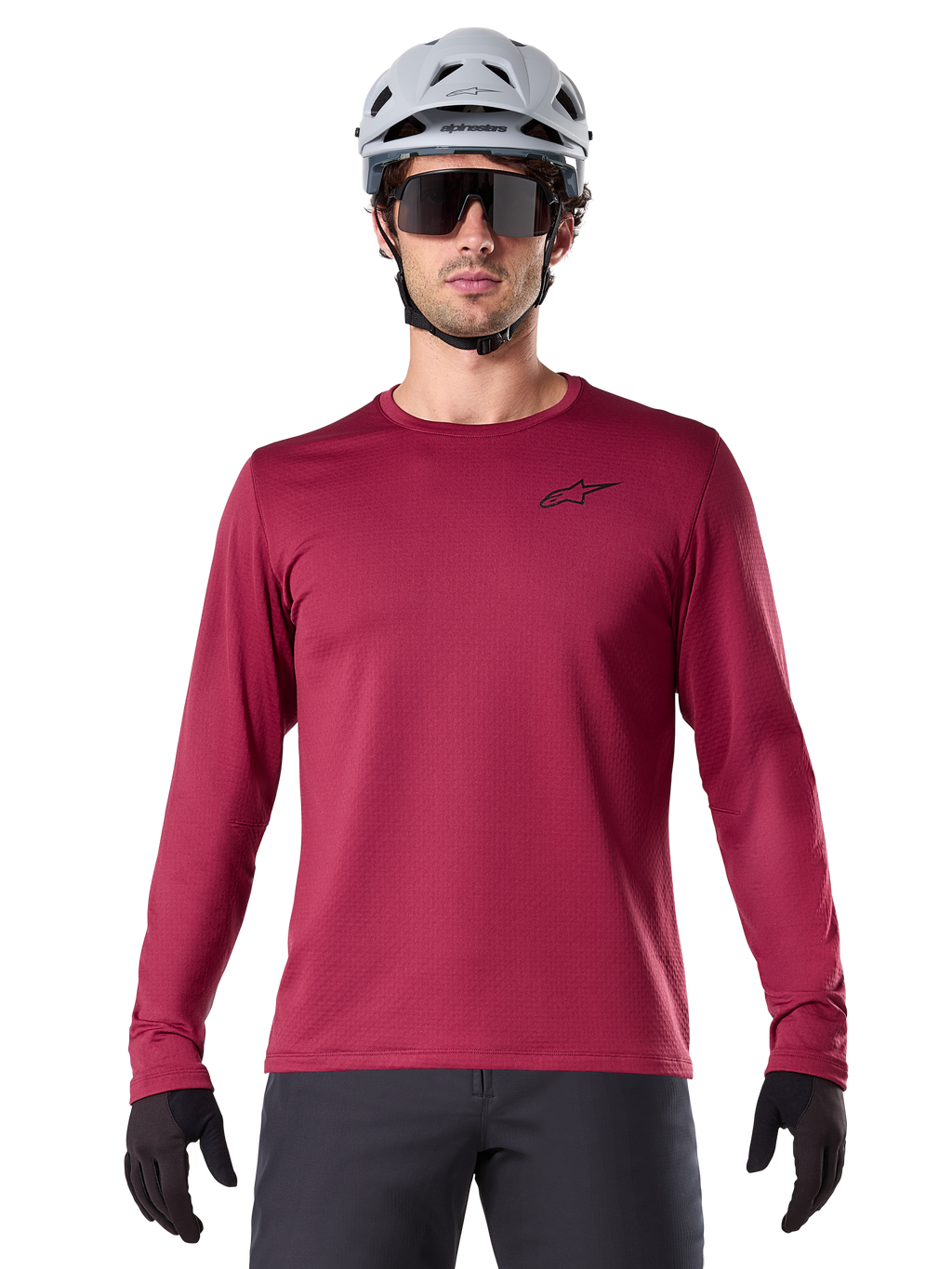 Male cyclist wearing Alpinestars A-Dura Thermal Jersey, Long Sleeve MTB Jersey, Burgundy, styled with a gray helmet and black sunglasses, features a small black star logo on the chest, insulated fleece fabric for cold-weather mountain biking