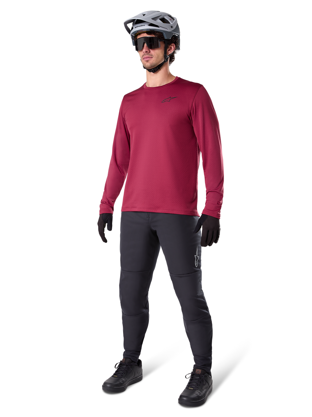 Alpinestars A-Dura Thermal Jersey in Burgundy, long-sleeve insulated cycling top worn with dark grey mountain bike pants, black gloves, and a grey helmet, full-body studio shot of cold-weather MTB gear.