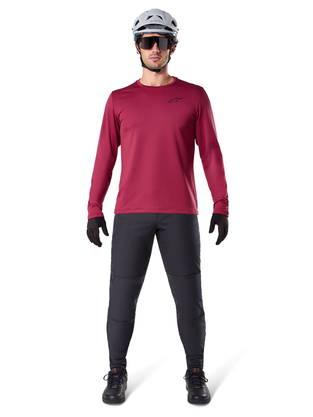 Male model wearing Alpinestars A-Dura Thermal Jersey in Burgundy, long-sleeve insulated cycling top, paired with dark grey mountain bike pants, white helmet, black sunglasses, and black gloves, professional MTB gear for cold weather