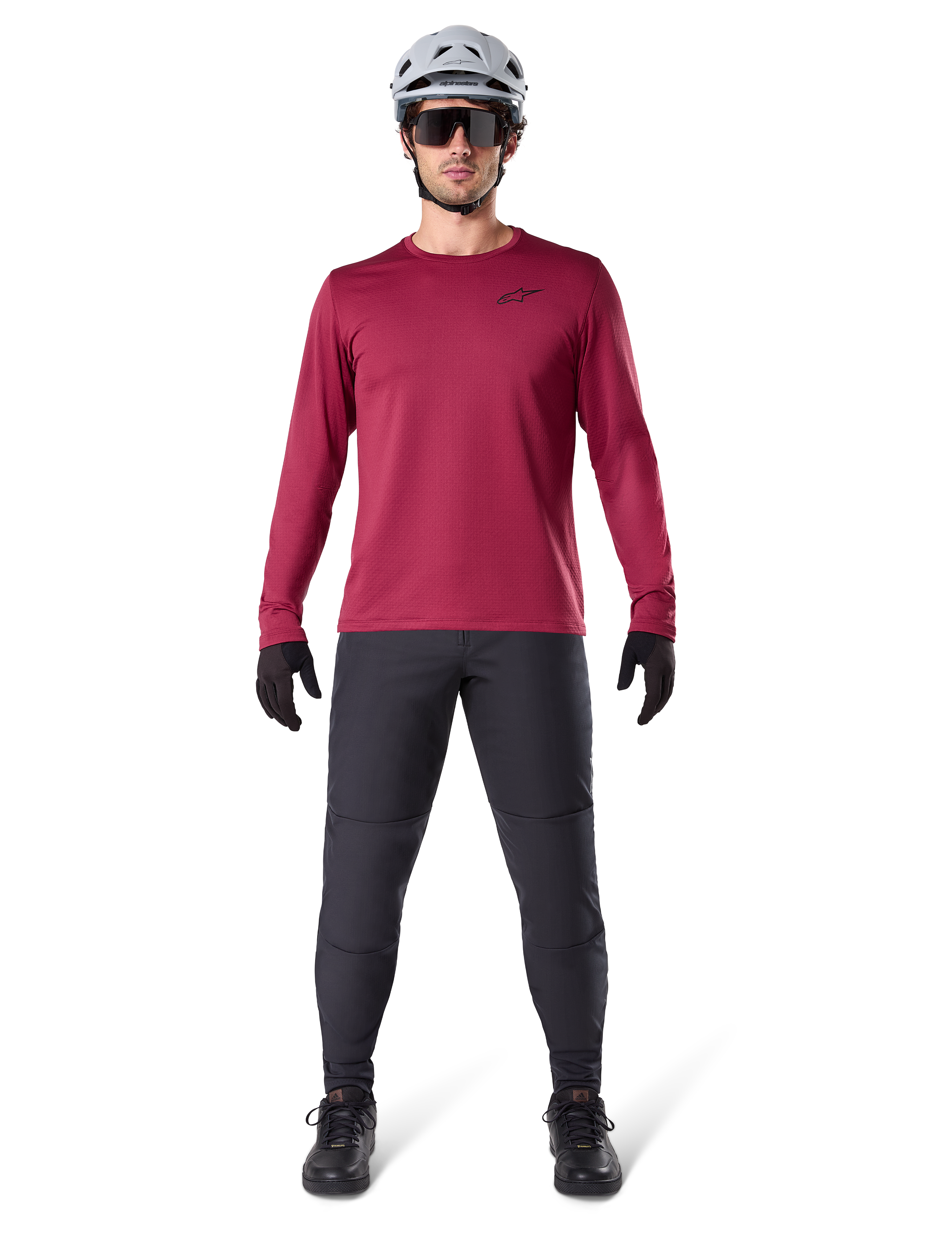 Male model wearing Alpinestars A-Dura Thermal Jersey in Burgundy, long-sleeve insulated cycling top, paired with dark grey mountain bike pants, white helmet, black sunglasses, and black gloves, professional MTB gear for cold weather