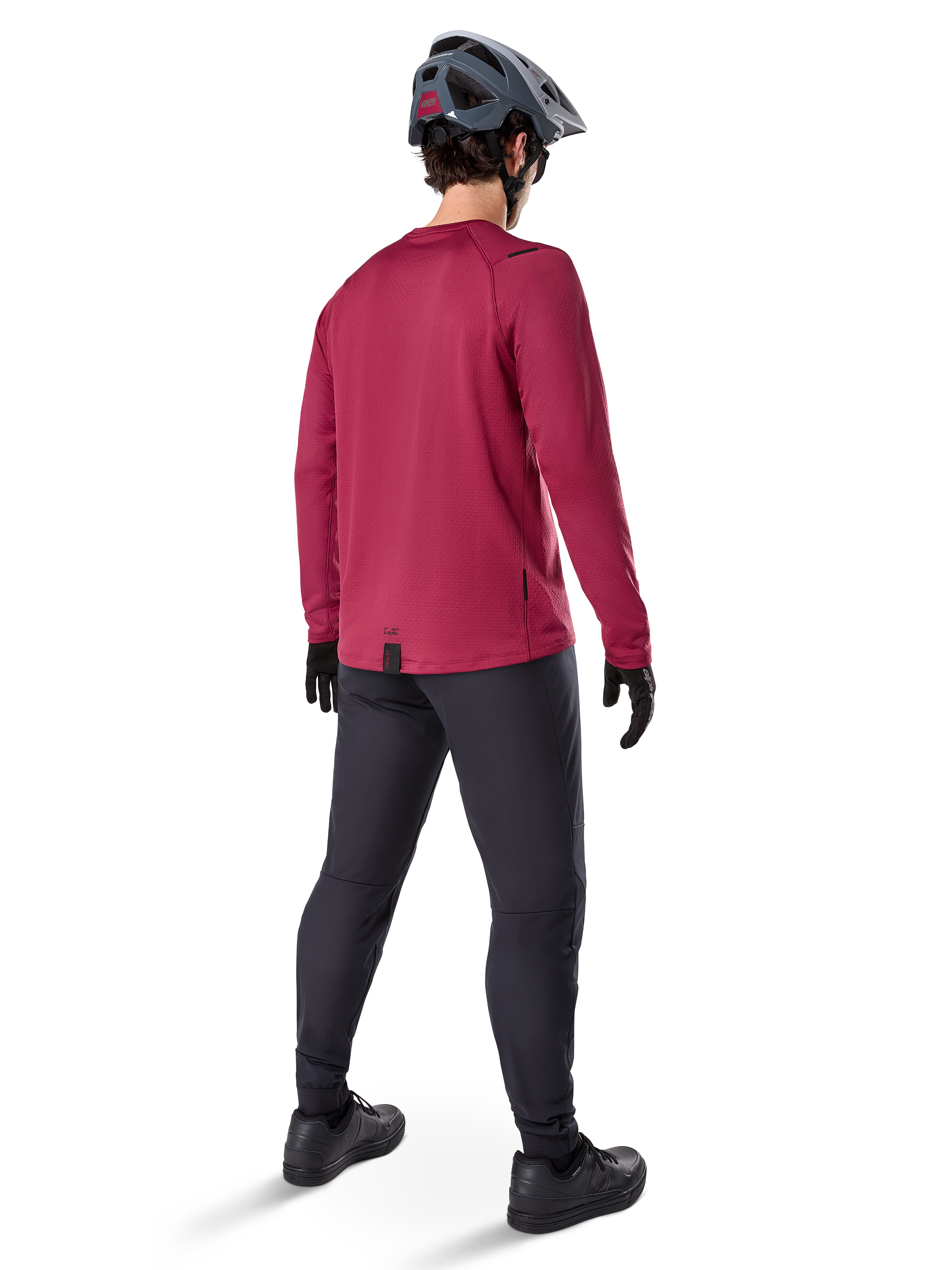 Alpinestars A-Dura Thermal Jersey, Burgundy long-sleeve cycling jersey, back view, worn with black mountain bike pants and a grey helmet, featuring an extended drop tail hem for rear coverage, mountain bike gear for cold weather