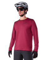Alpinestars A-Dura Thermal Jersey, Long-Sleeve Mountain Biking Jersey, Burgundy Red, featuring insulated fleece lining and small black chest logo, worn with a gray helmet, black sunglasses, and black gloves, designed for cold-weather cycling