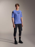Male model wearing Alpinestars A-Aria Elite Shorts in Black Titanium and A-Aria Polartec Elite SS Jersey in light purple, paired with black mountain bike knee pads and shoes, professional cycling gear for off-road performance.