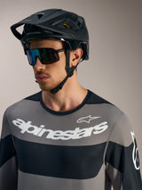 Alpinestars A-Dura Race Long Sleeve Jersey in gray with bold white logos, black MTB helmet, and performance sunglasses.