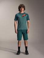 Alpinestars A-Dura Shorts in Dark Pine, men's mountain bike shorts, shown on a model with a matching teal short-sleeve jersey featuring a red and black star logo, black socks and cycling shoes, casual sporty mountain biking apparel