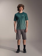 Male model wearing Alpinestars A-Dura Rise Jersey - Short Sleeve in Silver Pine, green cycling jersey with small white chest logo, paired with grey mountain bike shorts and black footwear, casual MTB trail gear