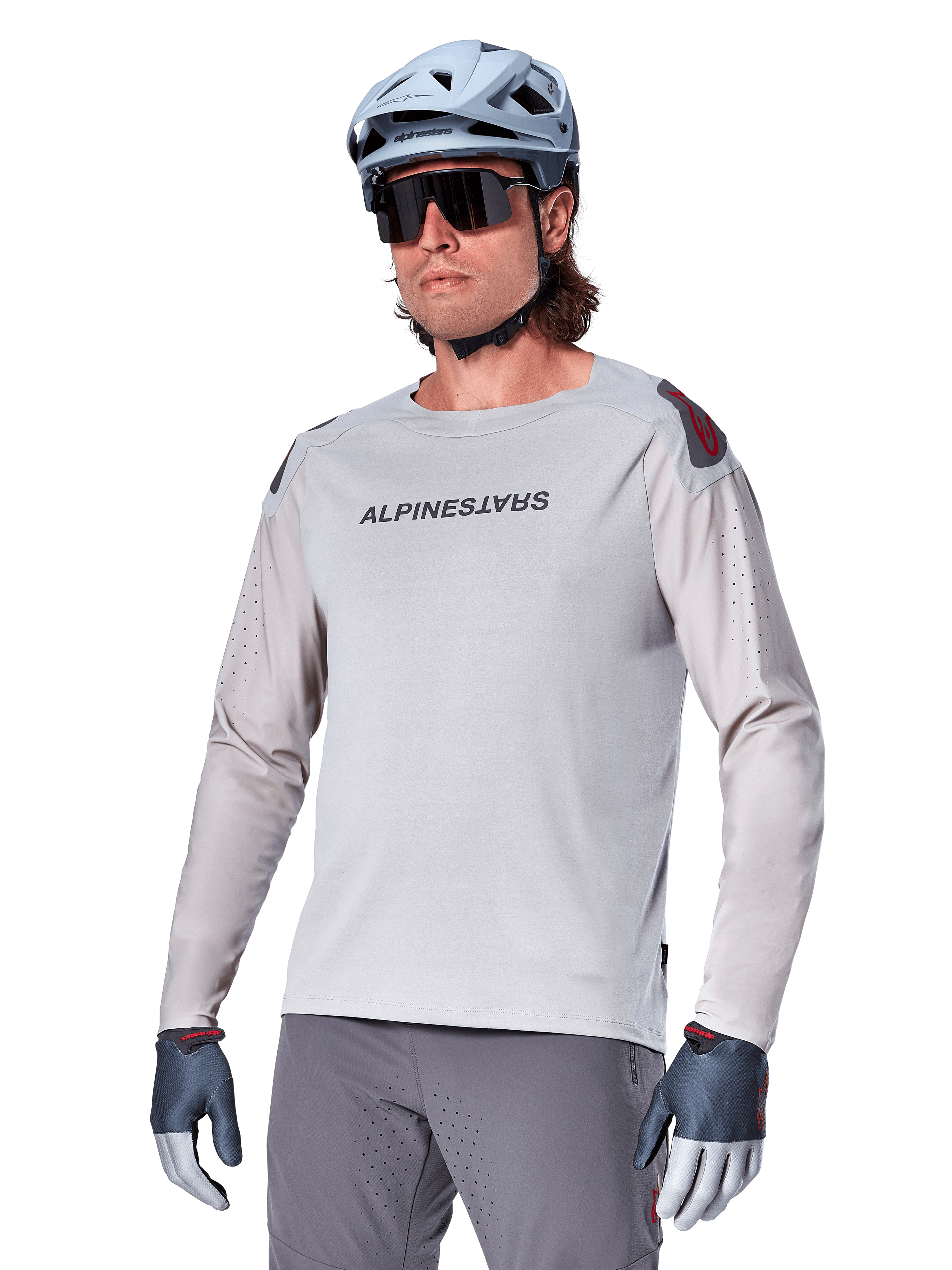 Alpinestars A-Aria Polartec Switch Jersey Long Sleeve, Light Gray cycling jersey with black chest logo and red shoulder accent, laser-perforated sleeves for airflow, worn with a light blue helmet, sunglasses, and gray pants, performance mountain bike apparel for trail riding