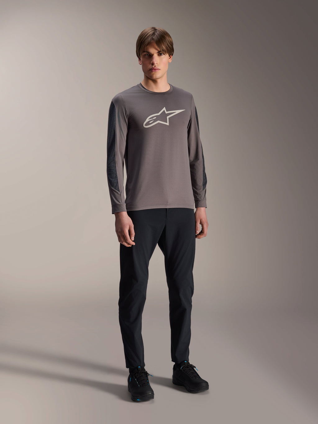 Alpinestars A-Dura Insert Astar Jersey, Long Sleeve MTB Jersey, Dark Gray, featuring large white chest logo, worn with black technical pants and black shoes, off-road cycling apparel