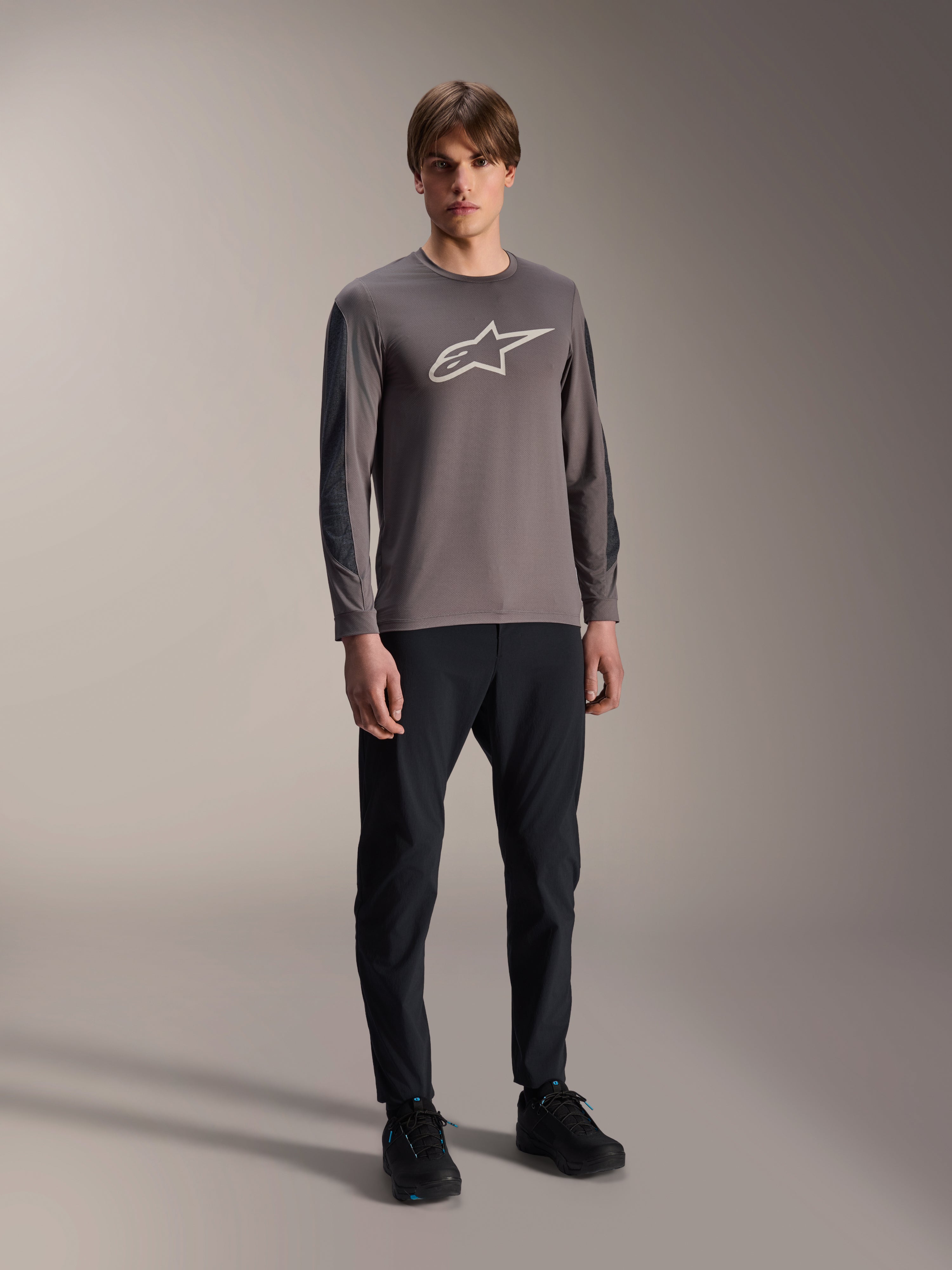 Alpinestars A-Dura Insert Astar Jersey, Long Sleeve MTB Jersey, Dark Gray, featuring large white chest logo, worn with black technical pants and black shoes, off-road cycling apparel