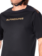 Alpinestars A-Aria Polartec Switch Jersey, Short Sleeve MTB Jersey, Black, Gold Alpinestars lettering on chest and logo on shoulder, close-up of the upper torso highlighting technical fabric and performance fit