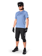 Male rider wearing the Alpinestars A-Dura Dri Astar Short Sleeve Jersey in Infinity Blue, paired with black MTB shorts, black helmet, sunglasses, knee pads, and gloves, complete mountain biking outfit