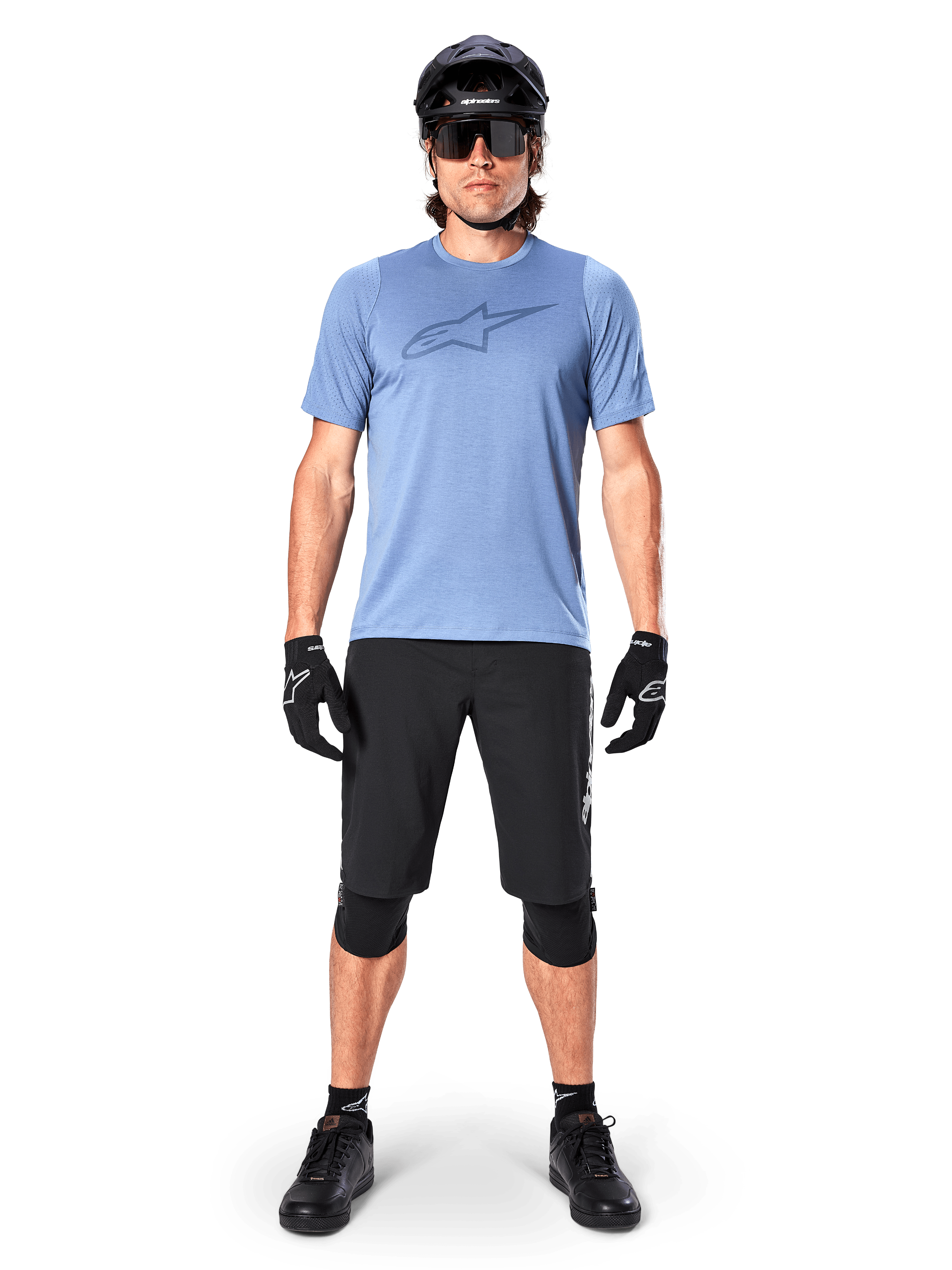 Male mountain bike rider wearing the Alpinestars A-Dura Dri Astar Short Sleeve Jersey in Infinity Blue, featuring a prominent Astars logo on the chest, coordinated with black MTB shorts, black helmet, sunglasses, and protective gear for off-road riding
