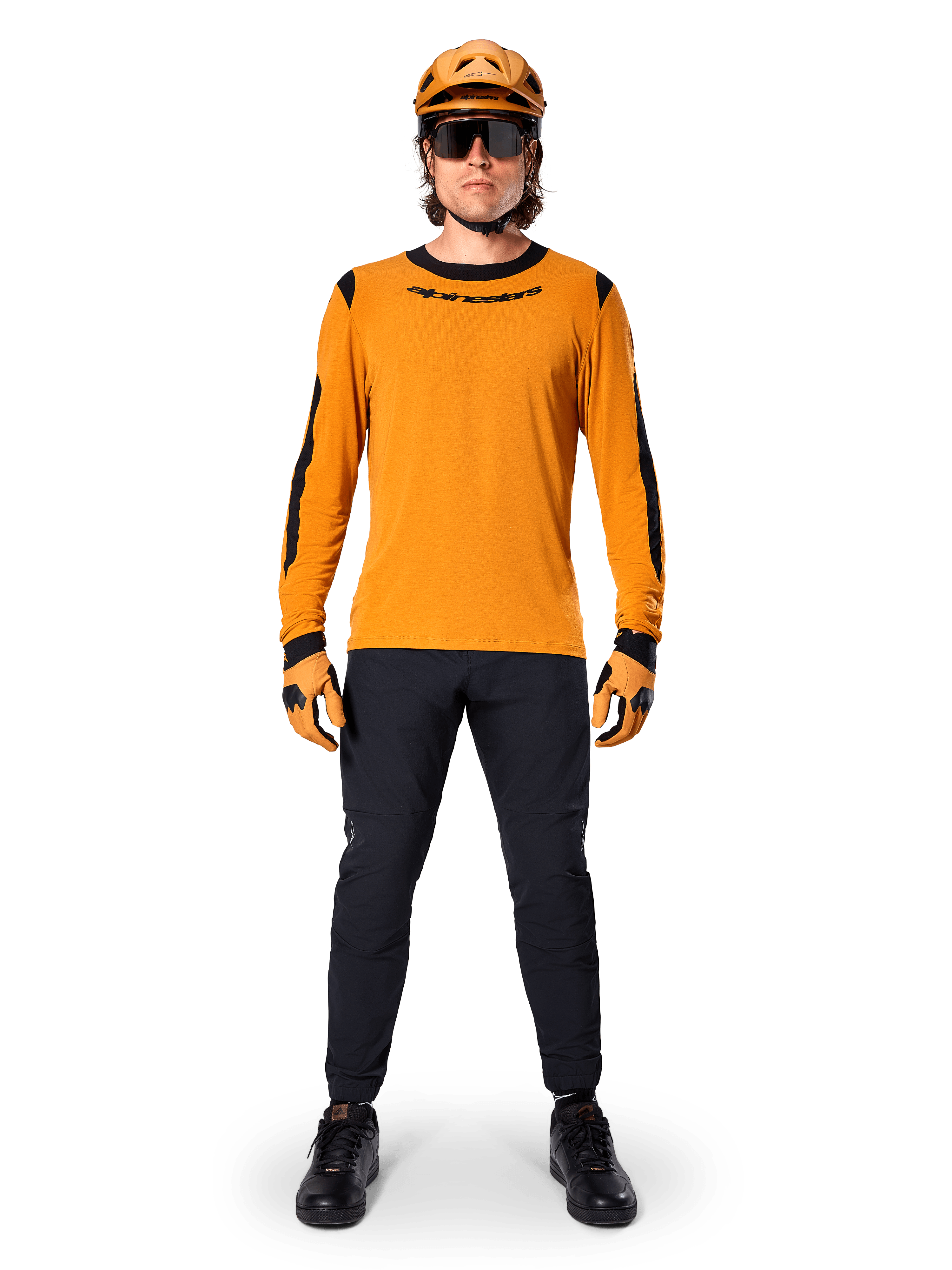 Mountain biker wearing Alpinestars A-Dura Dri Wool Long Sleeve Jersey, Dark Gold with black accents on neck and sleeves, paired with black pants, matching gold helmet, gloves, and black sunglasses, professional mountain biking gear
