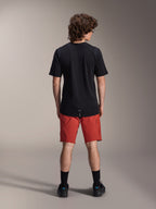 Male model wearing Alpinestars A-Dura Elite Shorts in Dark Orange and a black A-Dura Dri Wool Short Sleeve Jersey, seen from the back, paired with black socks and cycling shoes, professional mountain bike apparel