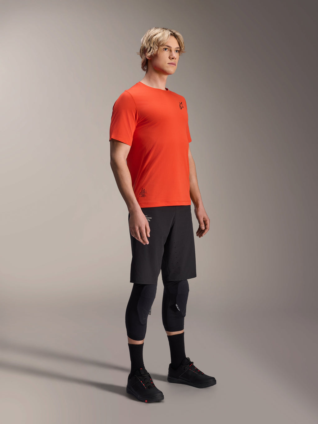 Alpinestars A-Aria Astar Short Sleeve Jersey in Spicy Orange, worn by a model with black MTB shorts and knee protection, lightweight breathable mountain bike apparel, vibrant orange with minimal black branding