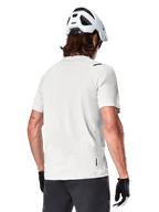 Alpinestars A-Aria Astar Jersey, Short Sleeve, White Dove, rear view of lightweight breathable mountain bike jersey, worn with a white helmet and black cycling gloves, featuring a dropped tail for extra coverage