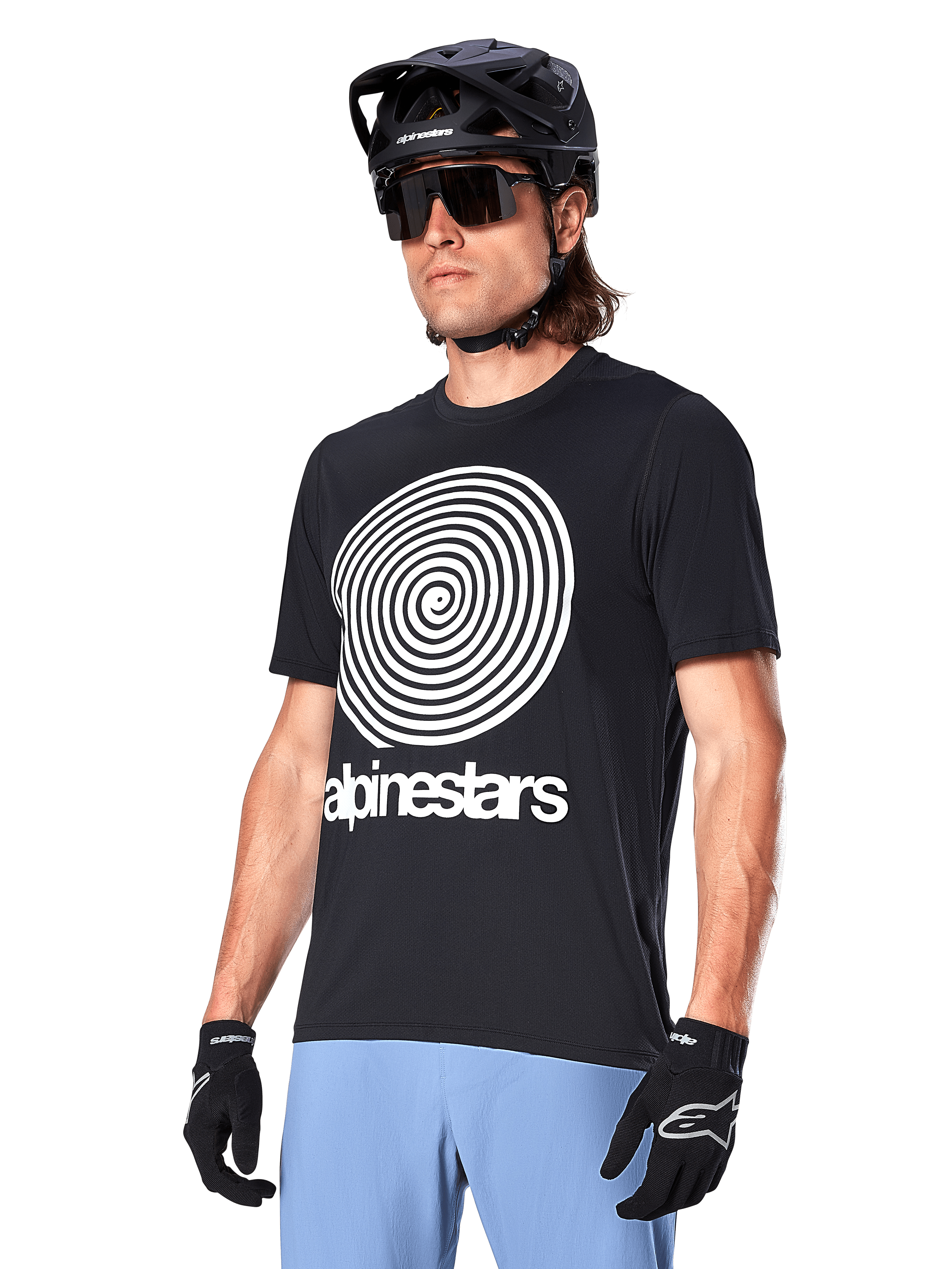 Alpinestars A-Dura Oscar Jersey - Short Sleeve, Black, featuring a large white spiral graphic and Alpinestars branding on the chest, worn by a rider with a black MTB helmet, sunglasses, and light blue pants