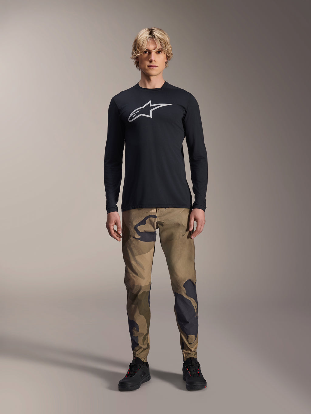 Alpinestars A-Dura Astar Long Sleeve Jersey, Black, featuring a large white Astars logo on the chest, worn with camouflage pants and black shoes, casual mountain bike performance wear