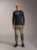 Alpinestars A-Dura Camo Pant, MTB Cycling Pants, Brown and Green Camouflage, worn with a black long-sleeve jersey and black shoes, sporty mountain bike style with durable stretch fabric