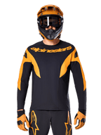 MTB rider wearing Alpinestars A-Supra Race Jersey - Long Sleeve, Black with orange graphics and chest logo, worn with matching orange full-face helmet, black goggles, and orange gloves, coordinated racing kit for mountain bike performance