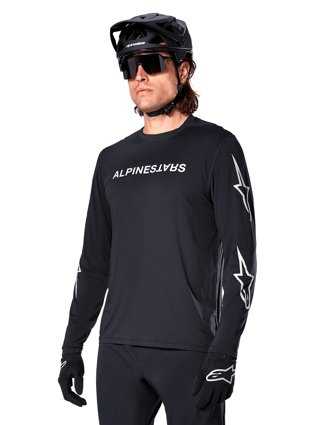 Male cyclist wearing Alpinestars A-Dura Switch Long Sleeve Jersey, Black with white wordmark and star logos on sleeves, styled with black MTB helmet and sunglasses, high-performance cycling gear for off-road riding