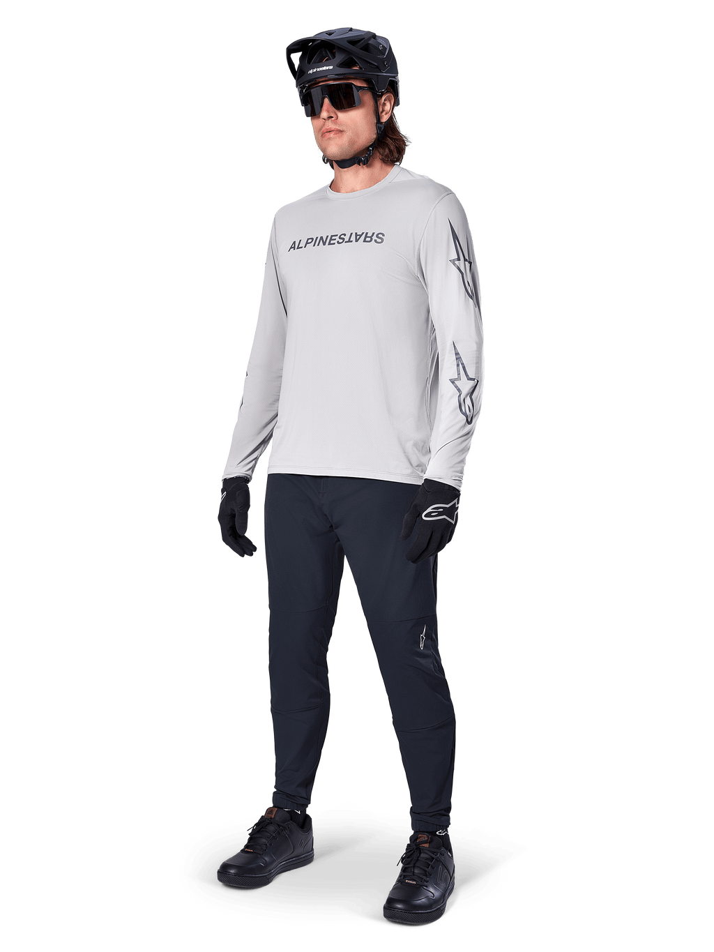 Alpinestars A-Dura Switch Long Sleeve Jersey, Light Gray, worn by male rider with black mountain bike pants and helmet, featuring black wordmark logo on chest and star graphics on sleeves, performance off-road cycling gear