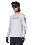 Alpinestars A-Dura Switch Long Sleeve Jersey, Mountain Bike Jersey, Light Gray, black wordmark screen print on chest and star logos on sleeves, worn with black mountain bike helmet, dark sunglasses, and black gloves, athletic off-road cycling gear