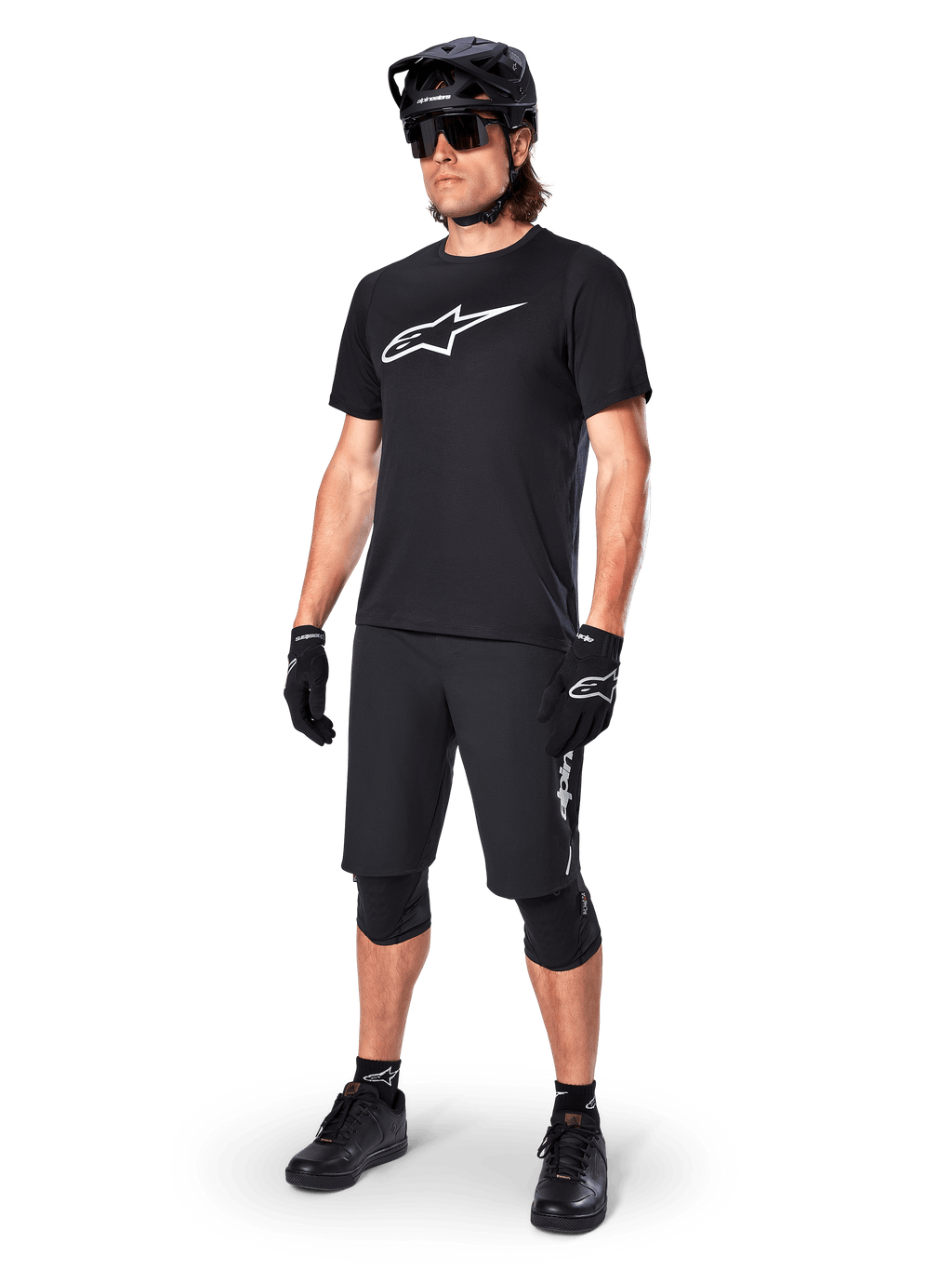 Mountain bike rider wearing the Alpinestars A-Dura Dri Oscar Short Sleeve Jersey in Black Reflective, featuring a large white logo on the chest, paired with matching black MTB shorts, gloves, and helmet, technical cycling apparel for off-road performance