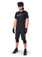 Mountain bike rider wearing the Alpinestars A-Dura Dri Oscar Short Sleeve Jersey in Black Reflective, featuring a large white logo on the chest, paired with matching black MTB shorts, gloves, and helmet, technical cycling apparel for off-road performance