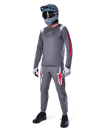 Alpinestars A-Supra Astar Long Sleeve Jersey in Dark Gray, featuring red branding on the sleeves and a white logo on the chest, worn by a rider with matching gray pants, a blue-gray full-face helmet, and performance gloves, coordinated mountain bike gear for gravity riding.