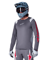 Alpinestars A-Supra Astar Long Sleeve Jersey, MTB Mountain Biking Jersey, Dark Gray with Red and White accents, performance fit, worn with matching gray pants featuring red and white star graphics, complete off-road cycling outfit with full-face helmet and gloves