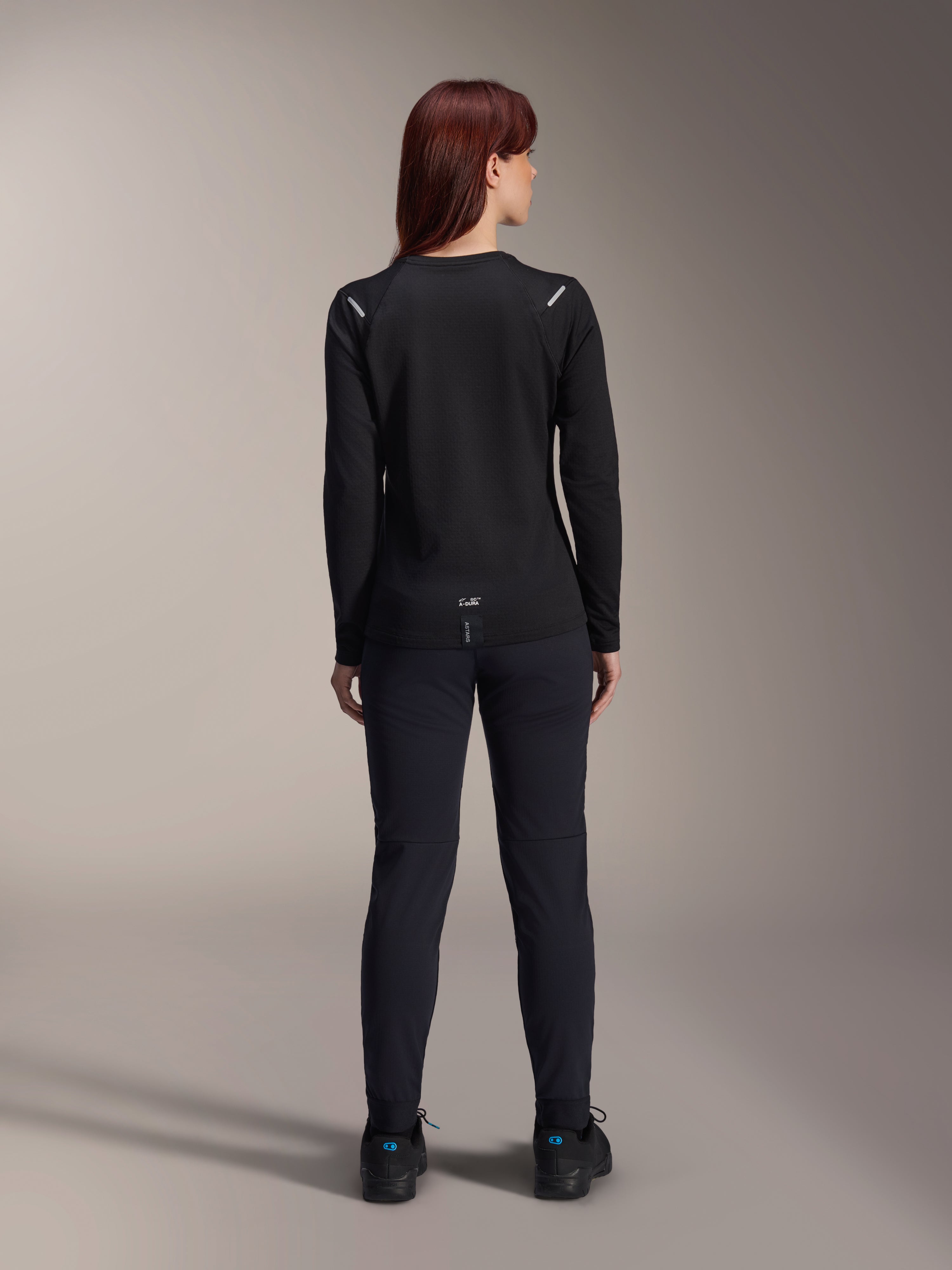 Alpinestars Woman Stella A-Dura Thermal Jersey, Back View, Black, Long-sleeve cycling jersey with insulated fleece, worn with matching black pants and shoes, featuring small A-Dura branding on the lower back and reflective shoulder accents, tailored for women's MTB riding.