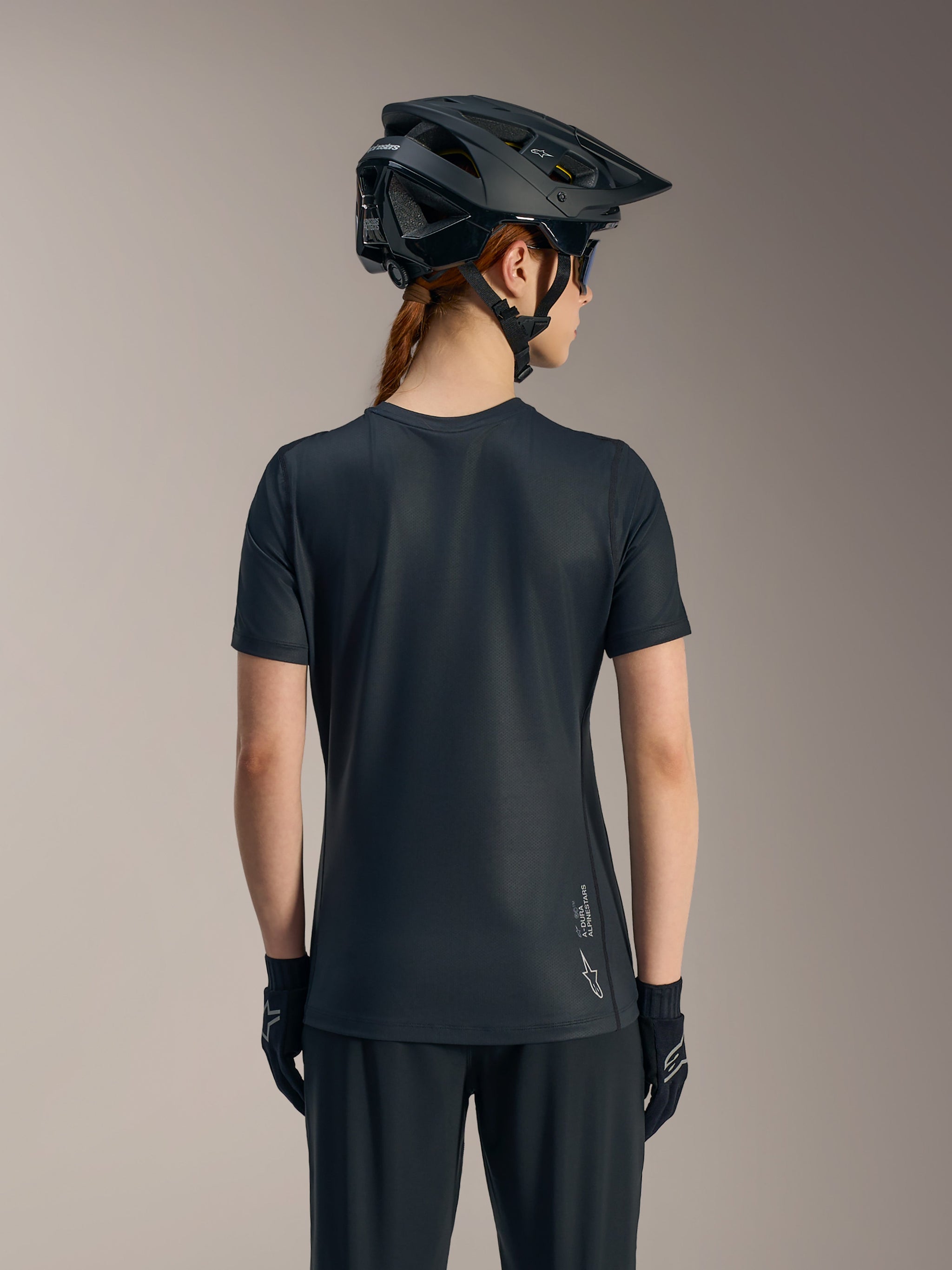 Black Stella A-Dura Ride Women's short sleeve jersey shown from behind, featuring a drop tail and Alpinestars logo.