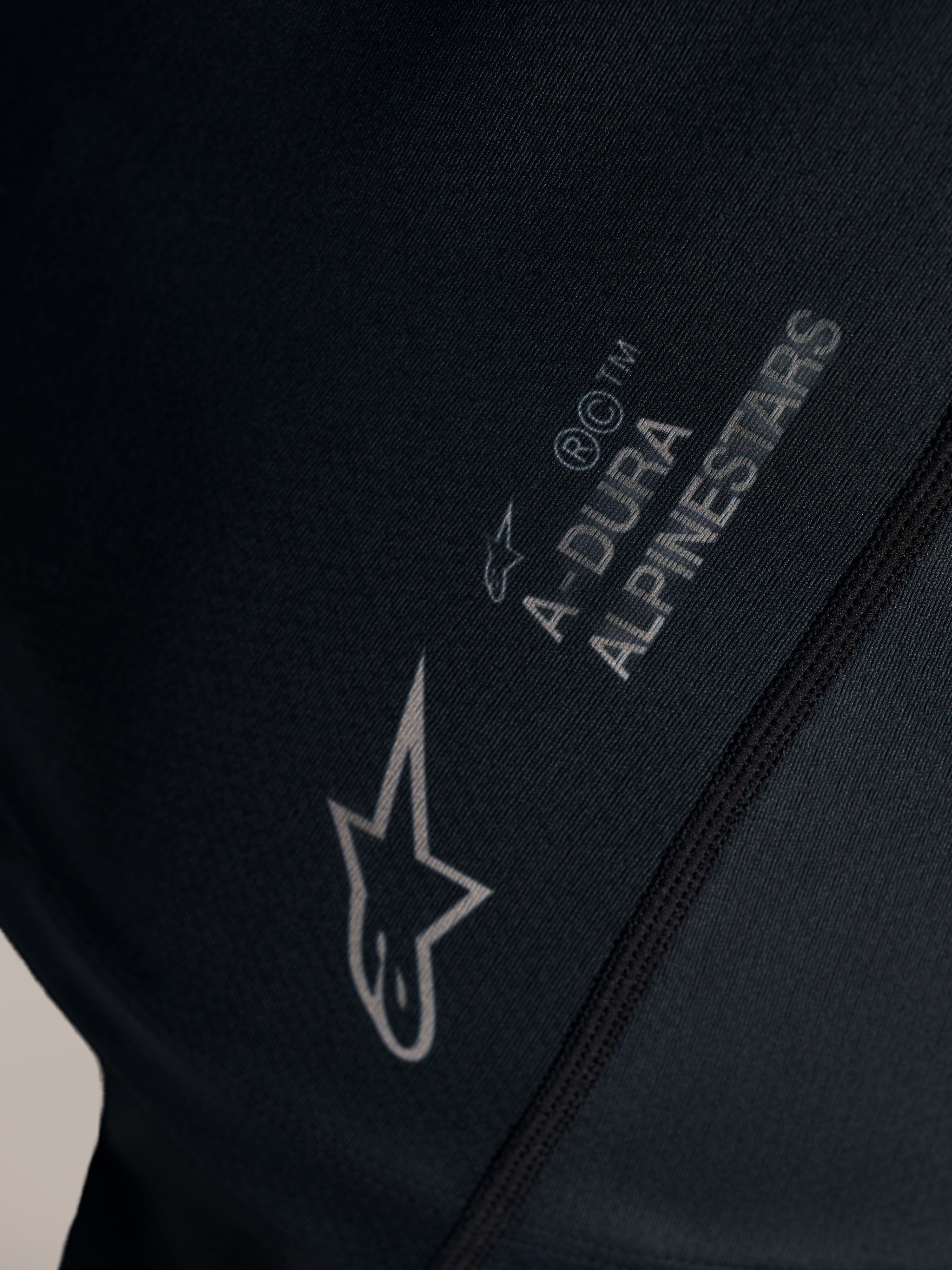 Close-up detail of black Stella A-Dura Ride Jersey with white Alpinestars logo and A-DURA branding on jacquard fabric.