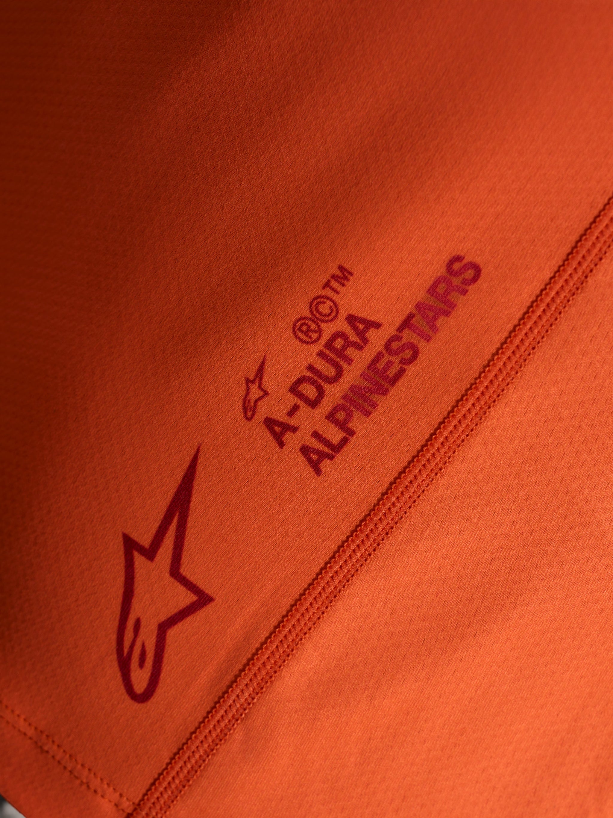 Orange Stella A-Dura Ride Jersey detail, featuring Alpinestars logo and A-DURA wordmark on technical stretch fabric.
