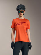 Orange Women's Stella A-Dura Ride short sleeve jersey with red logo, styled with black MTB helmet and sunglasses.